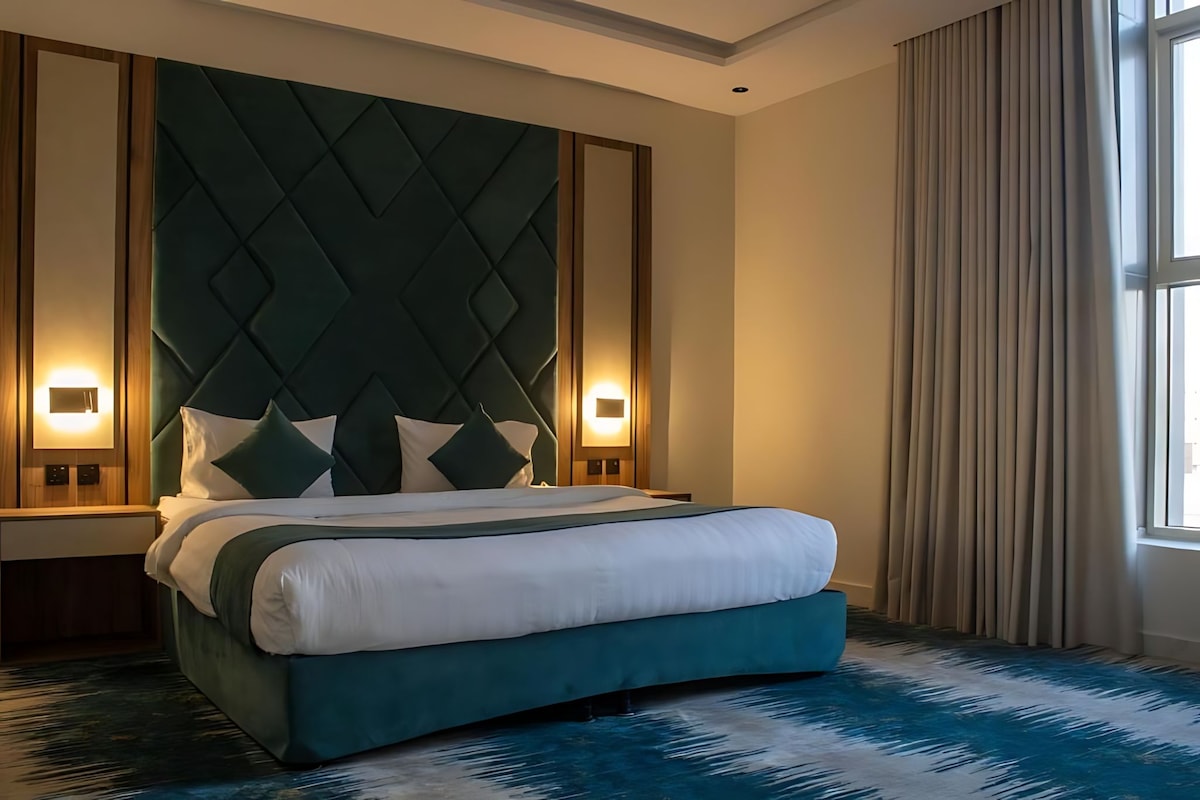 A hotel room with a large bed, two bedside tables, and a window with curtains.