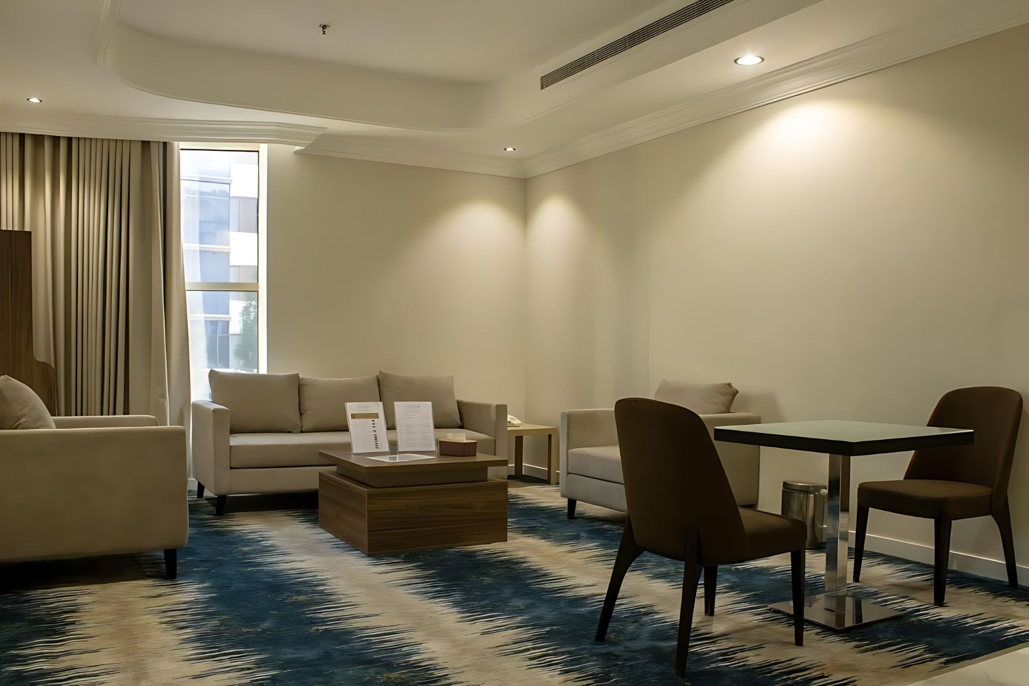 Ein modernes Hotelzimmer mit einer Couch, Sesseln, einem Esstisch und einem Couchtisch.