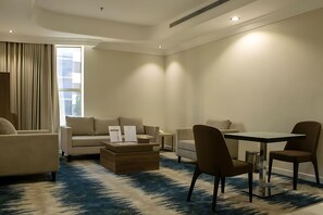 Una habitación de hotel moderna con sofá, sillones, una mesa de comedor y una mesa de centro.
