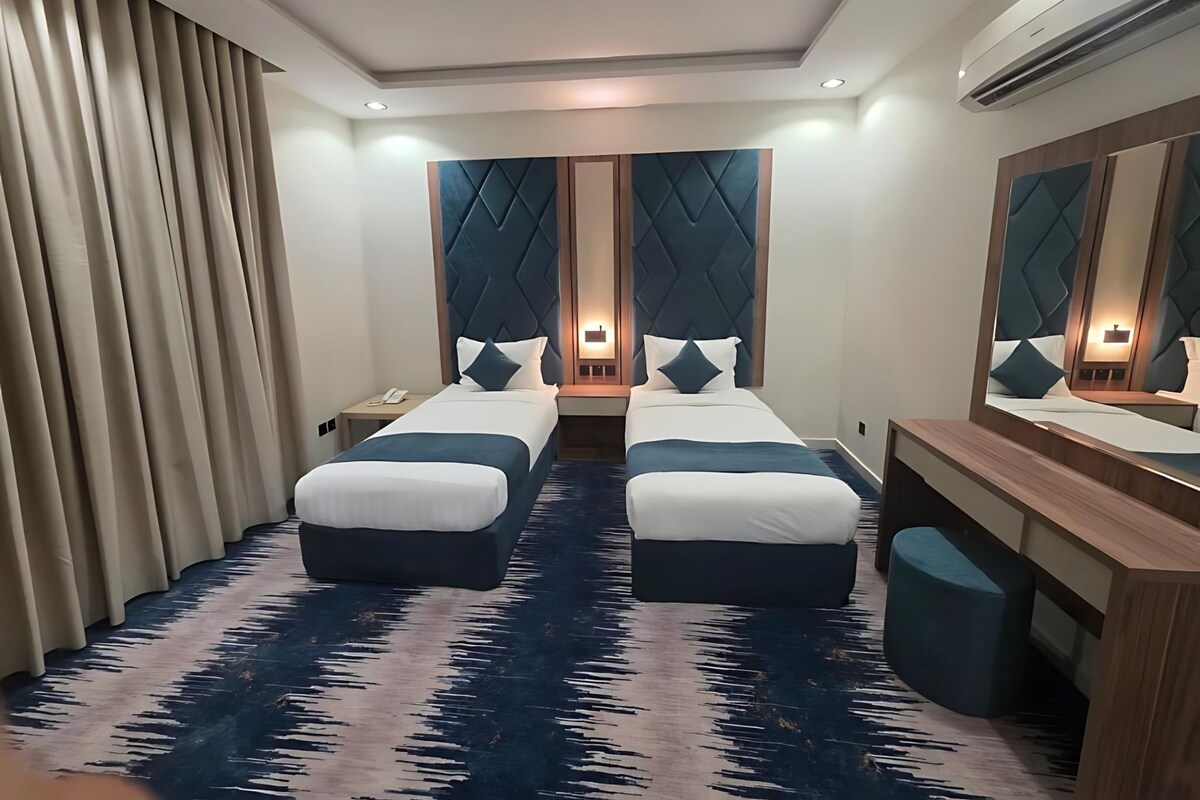 A hotel room with a large bed, a desk, a chair, and a mirror.
