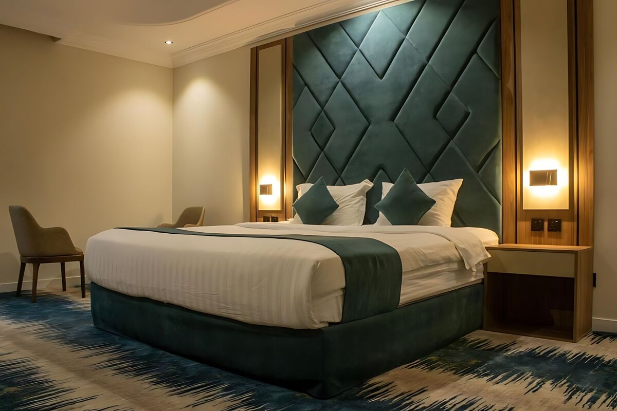 A hotel room with a large bed, two bedside tables, a chair, and a modern headboard.