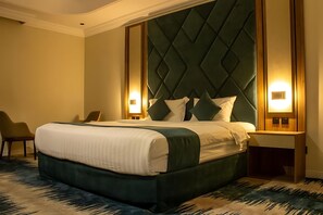 A hotel room with a large bed, a headboard with a diamond pattern, two bedside lamps, and a chair. - SOLEVA Serviced Apartments (Jeddah)