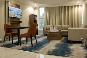 A modern living room with a flat-screen TV, two sofas, a coffee table, and a dining area with chairs. - SOLEVA Serviced Apartments (Jeddah)