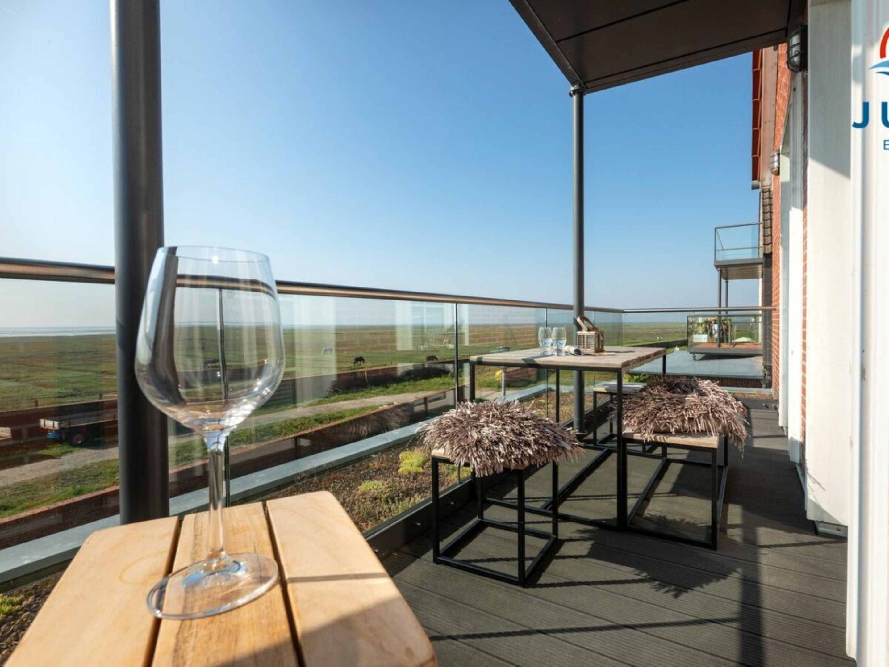 A balcony with a glass table and chairs, overlooking a landscape.