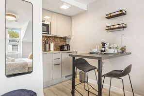 Une cuisine compacte dotée d’appareils électroménagers modernes, un coin repas avec des tabourets de bar et une vue sur l’extérieur par une fenêtre.