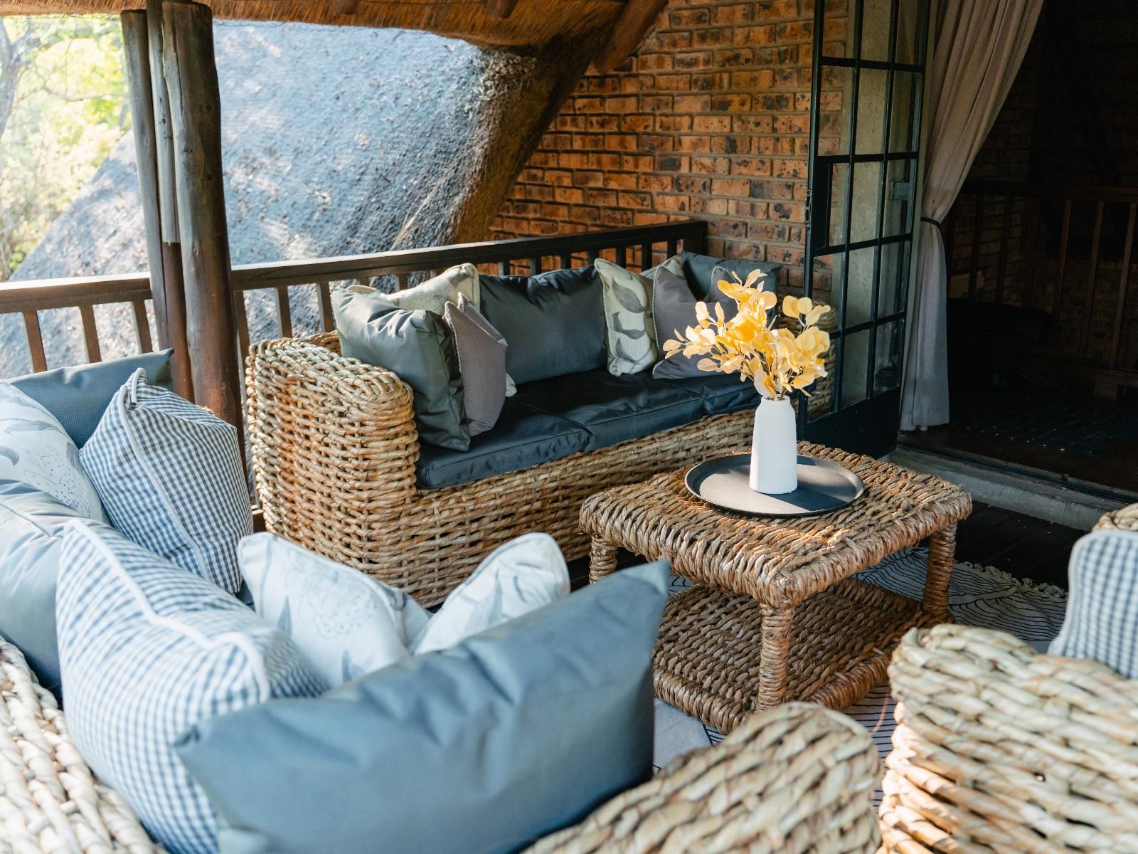 A wicker sofa with cushions, a small table with a vase, and a brick wall in the background.