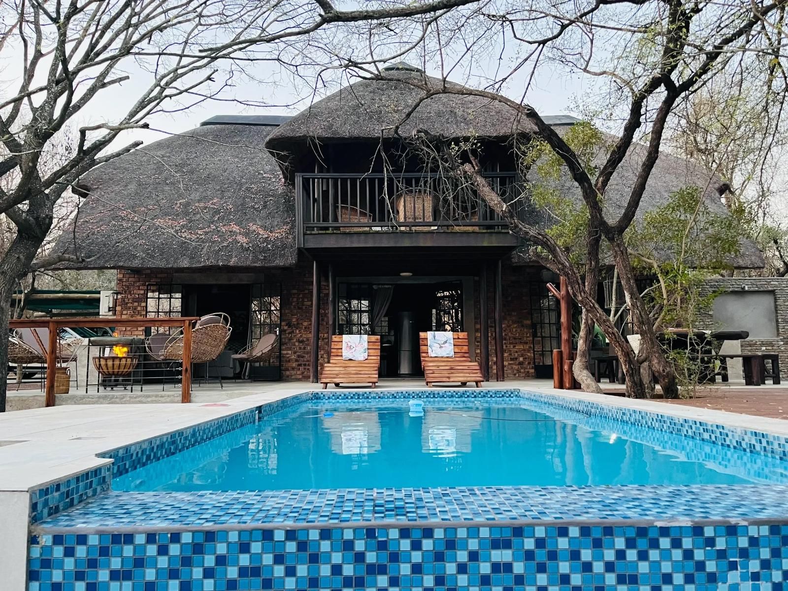 A pool area with a tiled deck, a building with a thatched roof, and a balcony overlooking the pool.