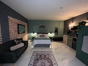A bedroom with a bed, a sofa, a kitchen area, and a bathroom.