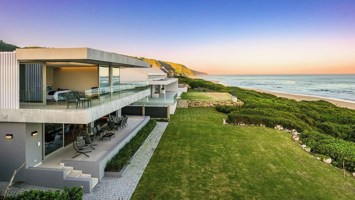 Une propriété moderne située en bord de mer, dotée d’une architecture à plusieurs niveaux, d’un espace extérieur aménagé et offrant une vue sur l’océan.