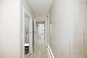 Un couloir étroit aux murs blancs et au plancher en bois.