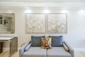Un salon moderne avec un canapé gris, deux coussins et deux œuvres d’art fixées au mur, représentant des motifs floraux.