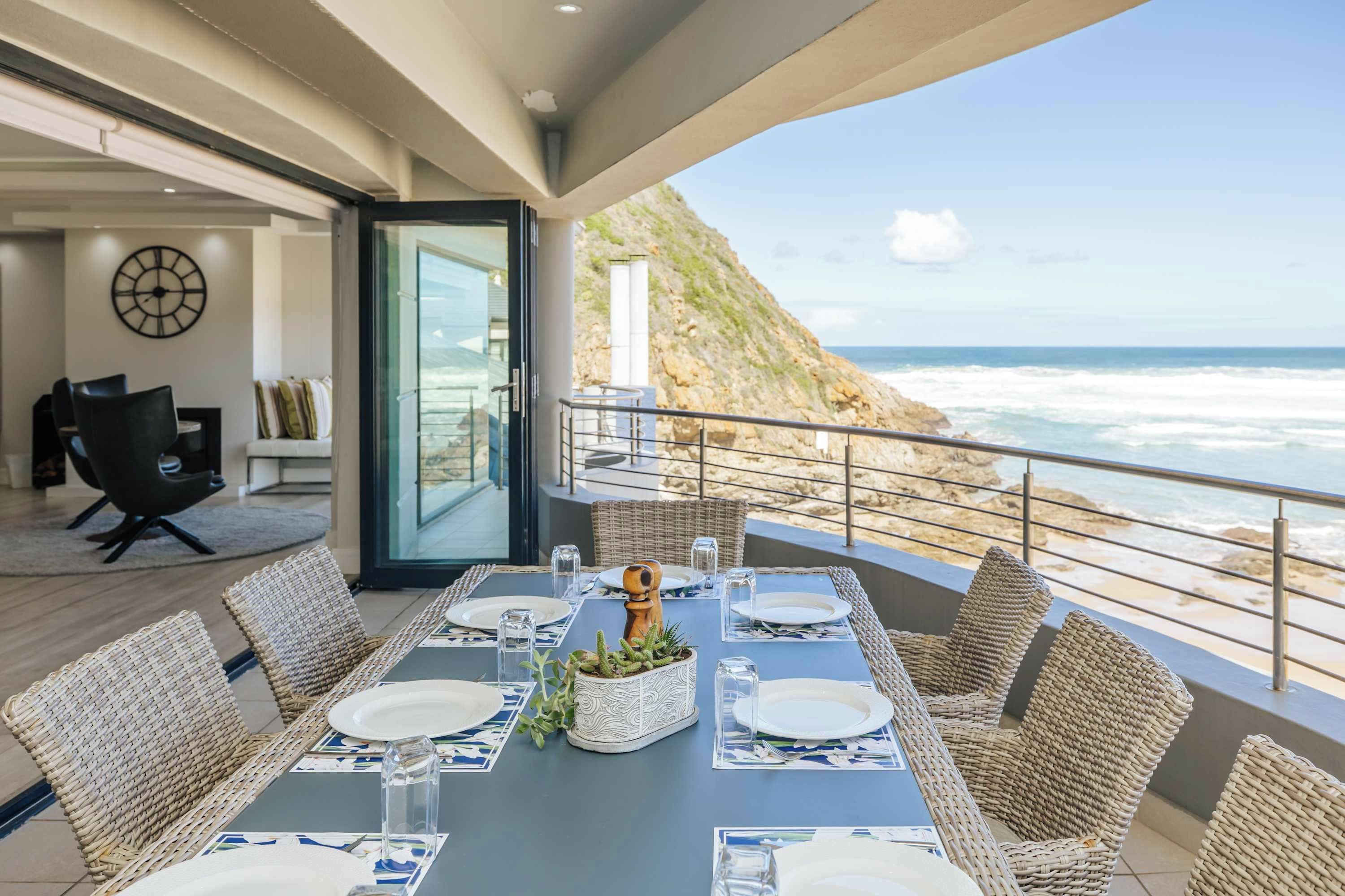 Un espace repas offrant une vue sur l’océan, un balcon avec des fauteuils en osier et un aménagement intérieur moderne.