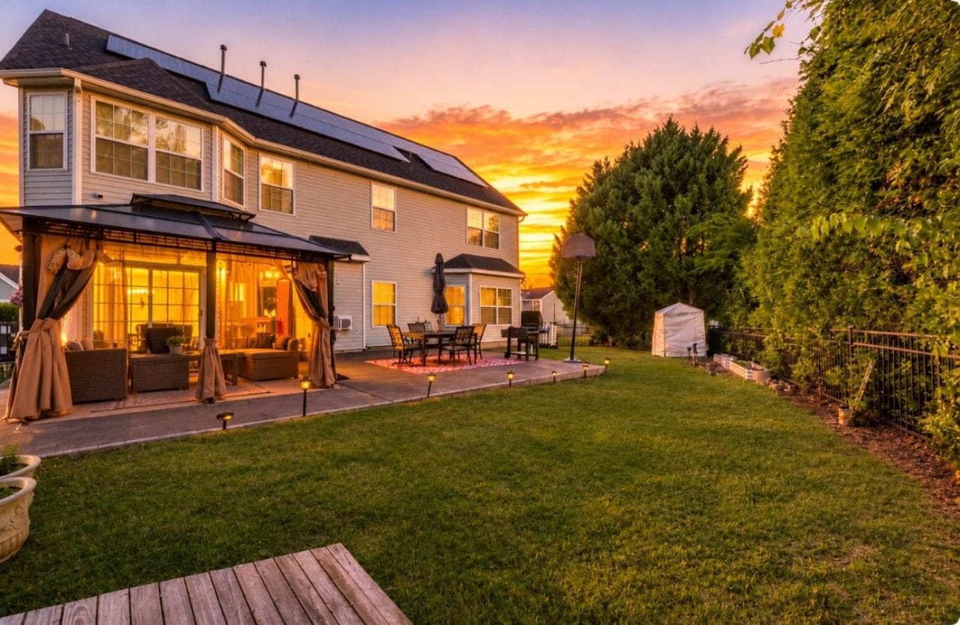 A residential house with a covered patio, a lawn, and a sunset in the background.