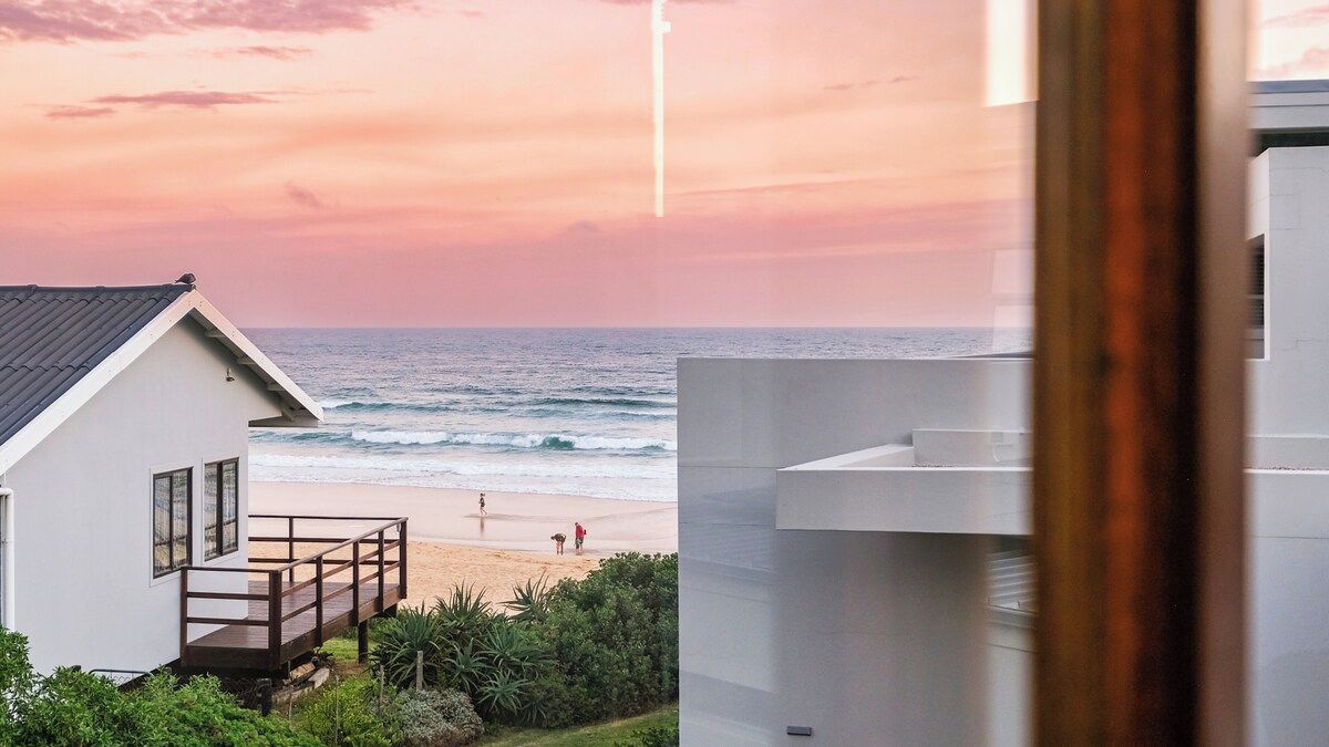 Une vue sur la côte, avec une plage, une maison dotée d’un balcon et un bâtiment moderne.