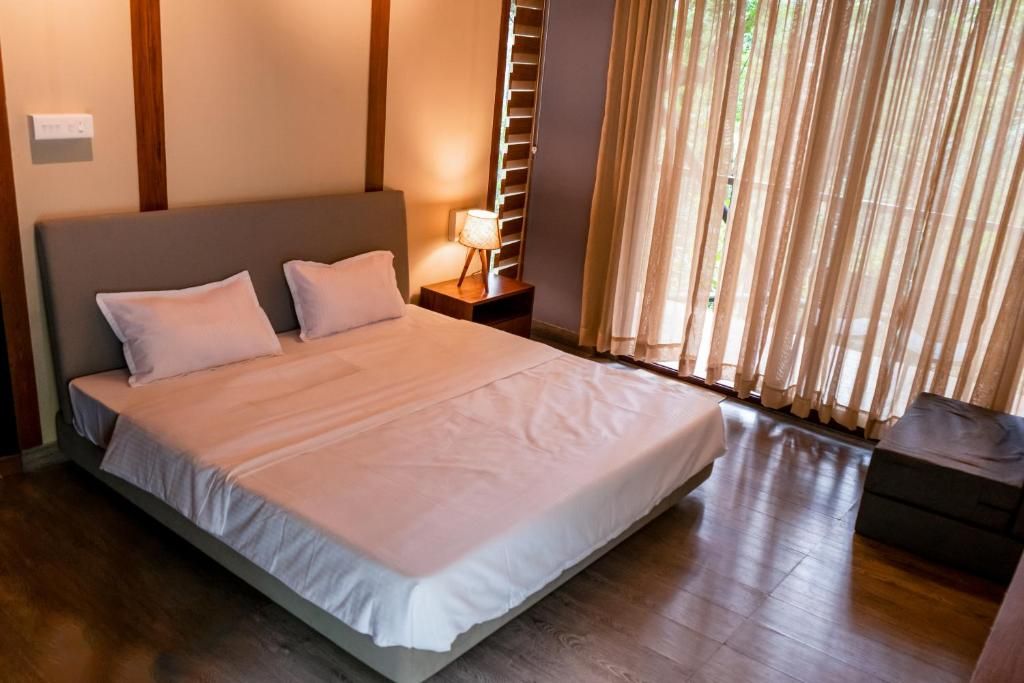 Une chambre à coucher avec un grand lit, une table de chevet avec une lampe et une fenêtre avec des rideaux.