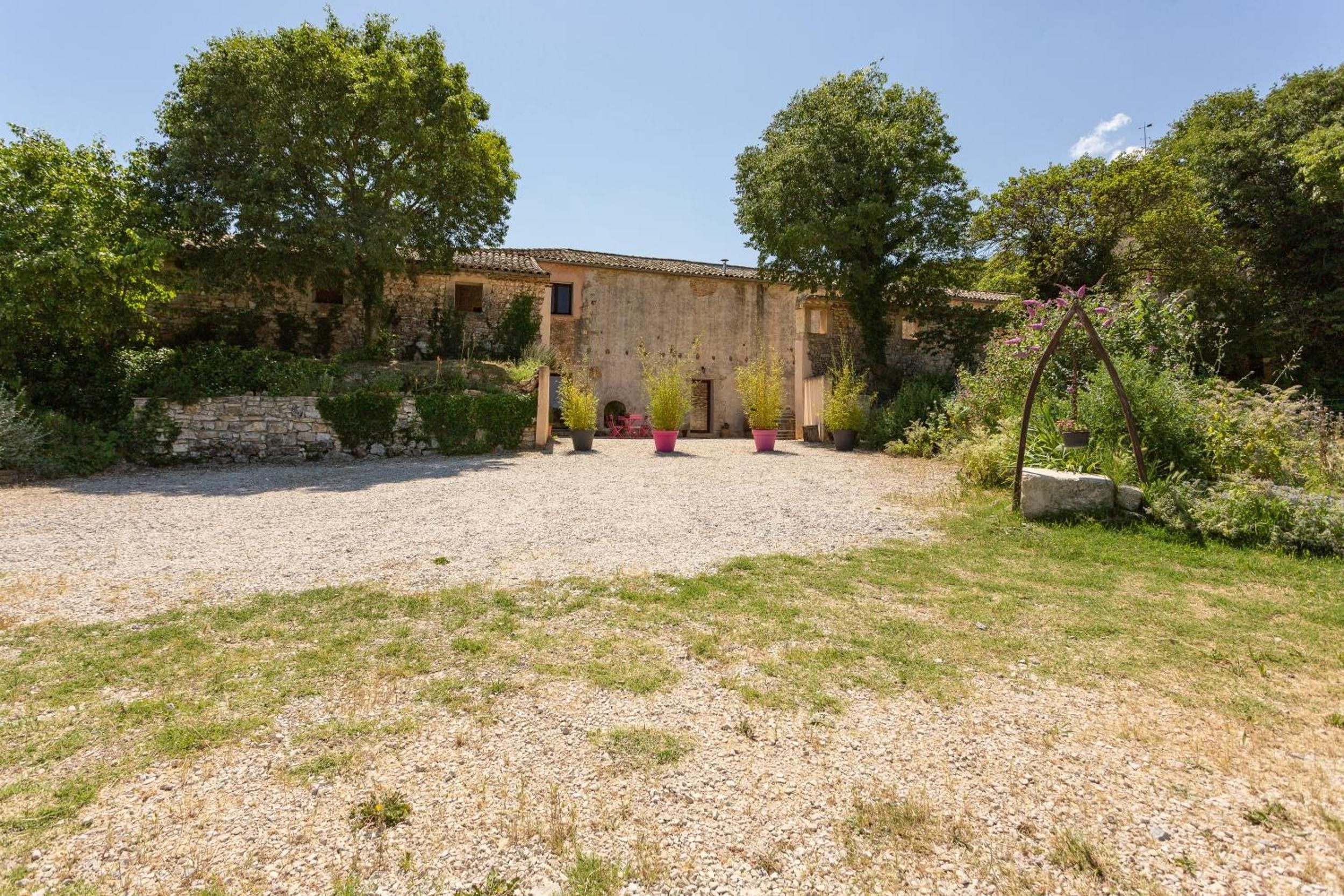 A rustic building with a gravel courtyard, surrounded by greenery and stone walls.