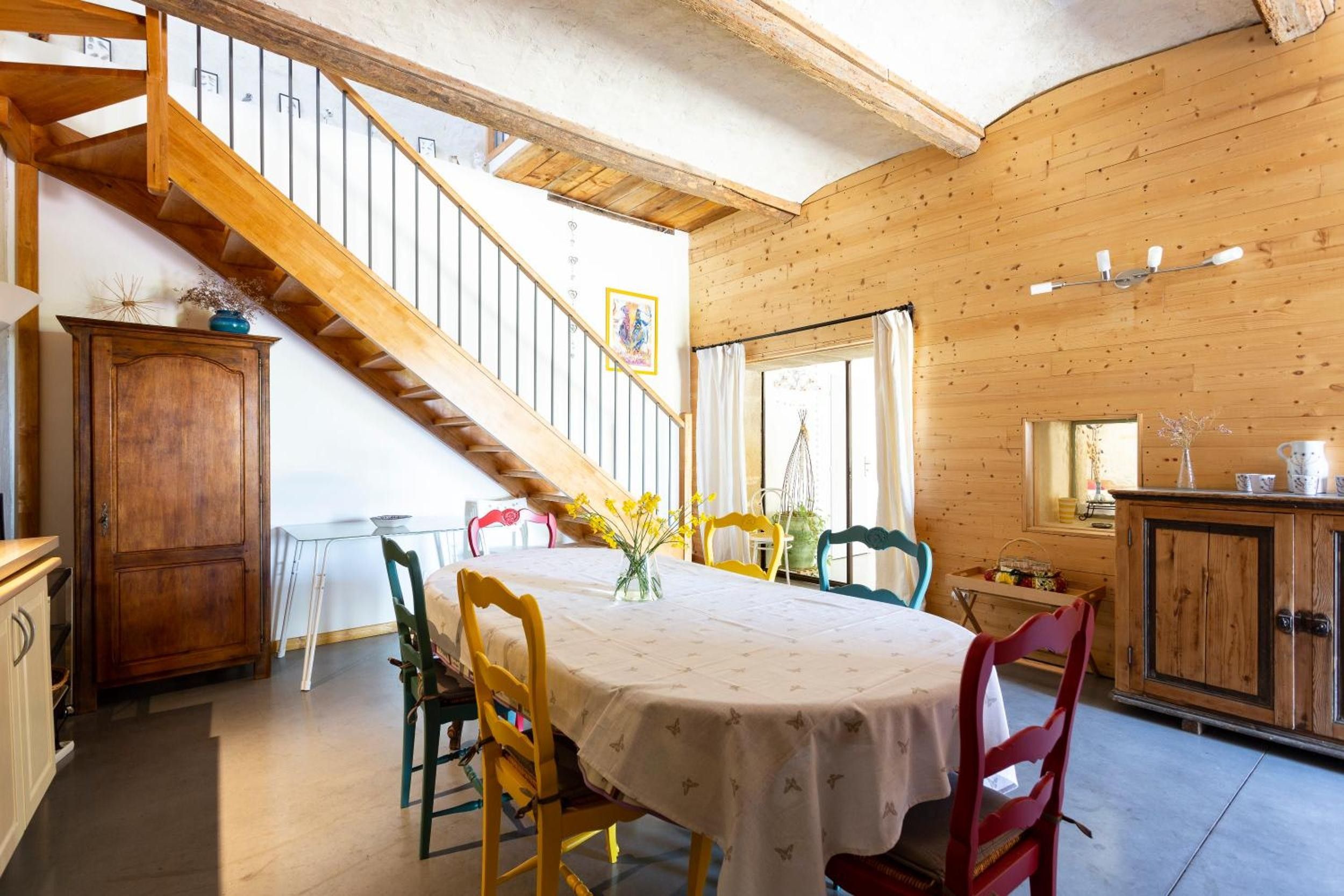 Un comedor con escalera de madera, una mesa con sillas y vistas al exterior.