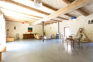 A spacious room with a high ceiling, exposed wooden beams, a fireplace, and a dining table with chairs.