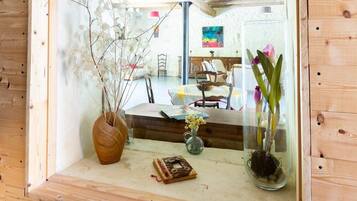 A wooden-framed mirror reflecting a room with a bed, a chair, and a vase with flowers.