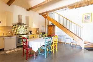 A kitchen with a dining area, wooden staircase, and a tiled backsplash.