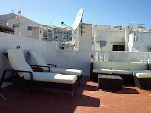 Eine Dachterrasse mit Liegestühlen, einer Couch, Satellitenschüsseln und einem Gebäude im Hintergrund.