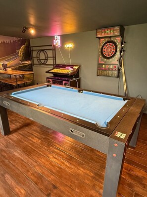A pool table with a dartboard and a jukebox in a room with wooden flooring. - Au Vieux Fourneau (Izier, Durbuy) (Durbuy)