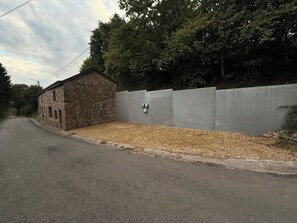 Ein Steinhaus neben einer Betonmauer mit einem Kiesweg davor.