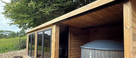 A wooden cabin with a hot tub, a deck, and a glass door leading to the interior.