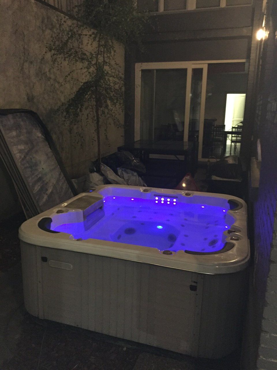 A hot tub with a blue light feature, located in an outdoor setting with a stone wall and a door in the background.