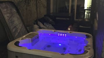 A hot tub with a blue light feature, located in an outdoor setting with a stone wall and a door in the background.