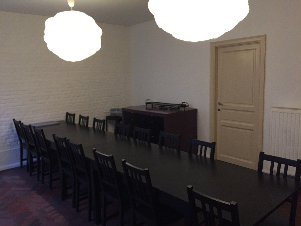A conference room with a long table and chairs, a white brick wall, a door, and a radiator.