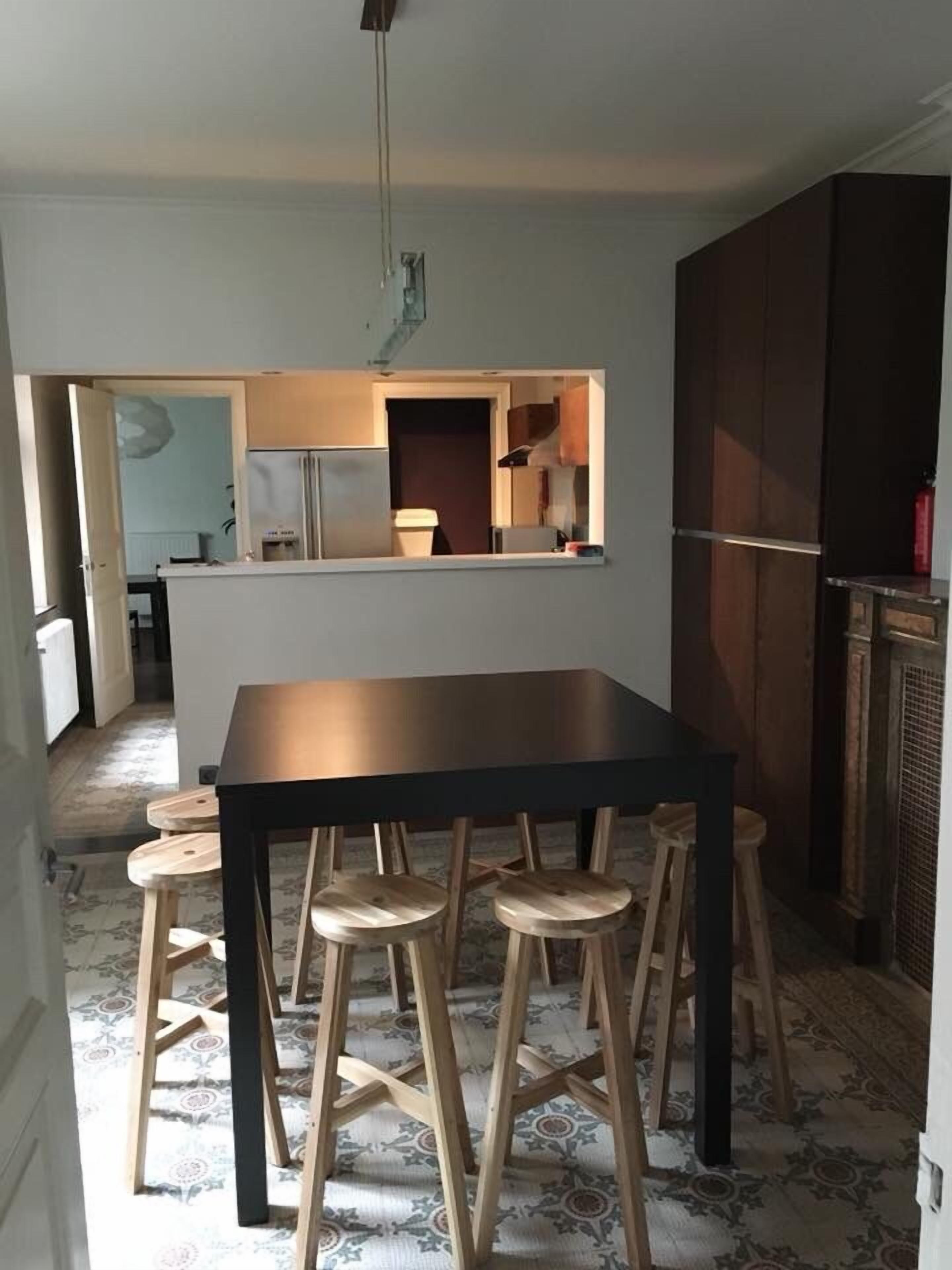 A dining area with a table and stools, a kitchen in the background, and patterned flooring.