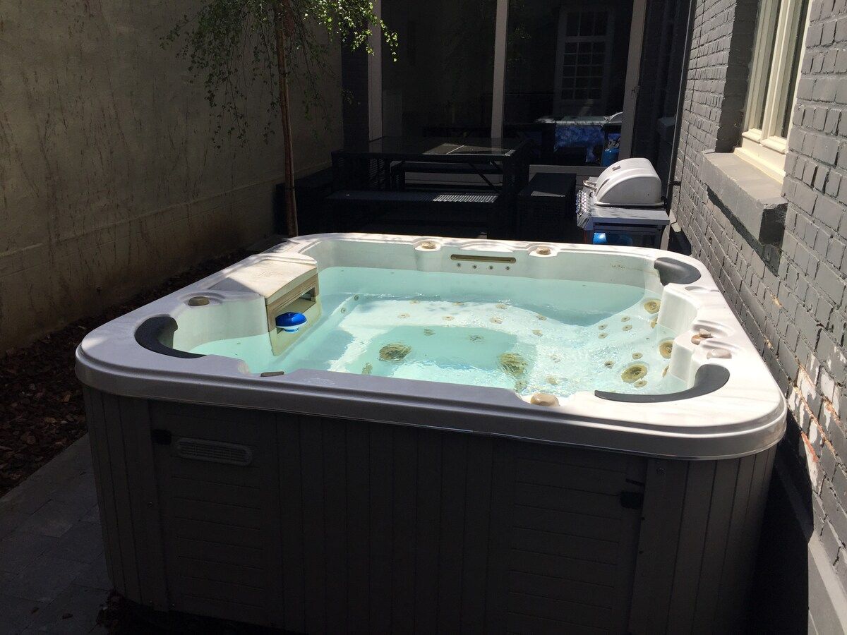 A hot tub in an outdoor setting with a brick wall and a window in the background.