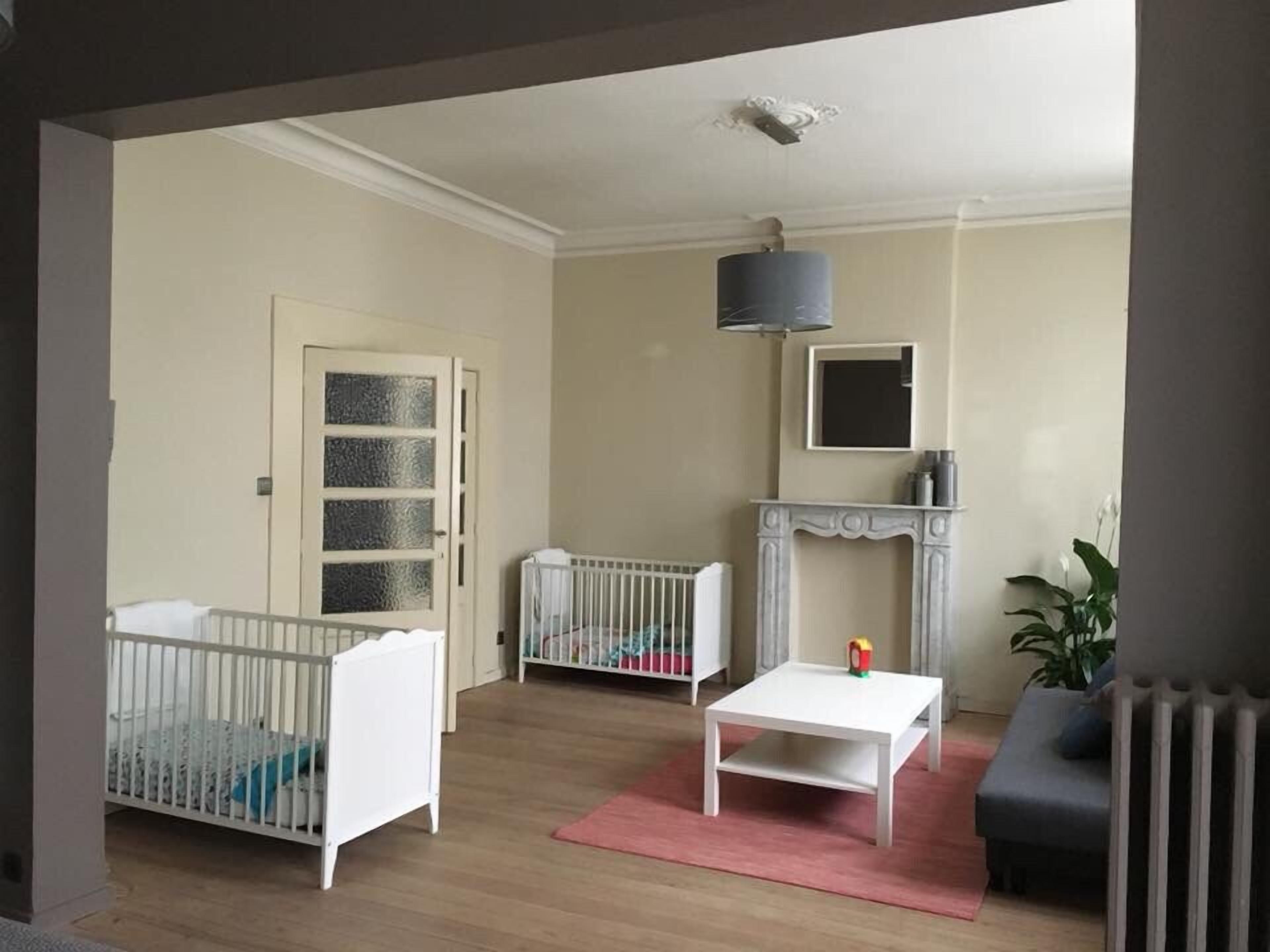 Una stanza con due lettini per bambini, un tavolo bianco, un camino e un termosifone.