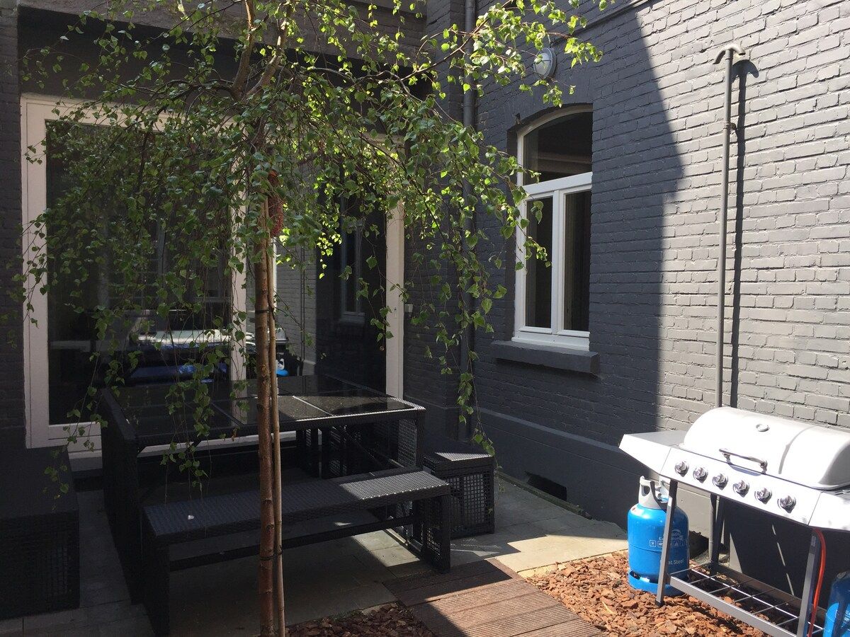 Eine Außenpatio mit Grill, Sitzgelegenheit und einem Baum.