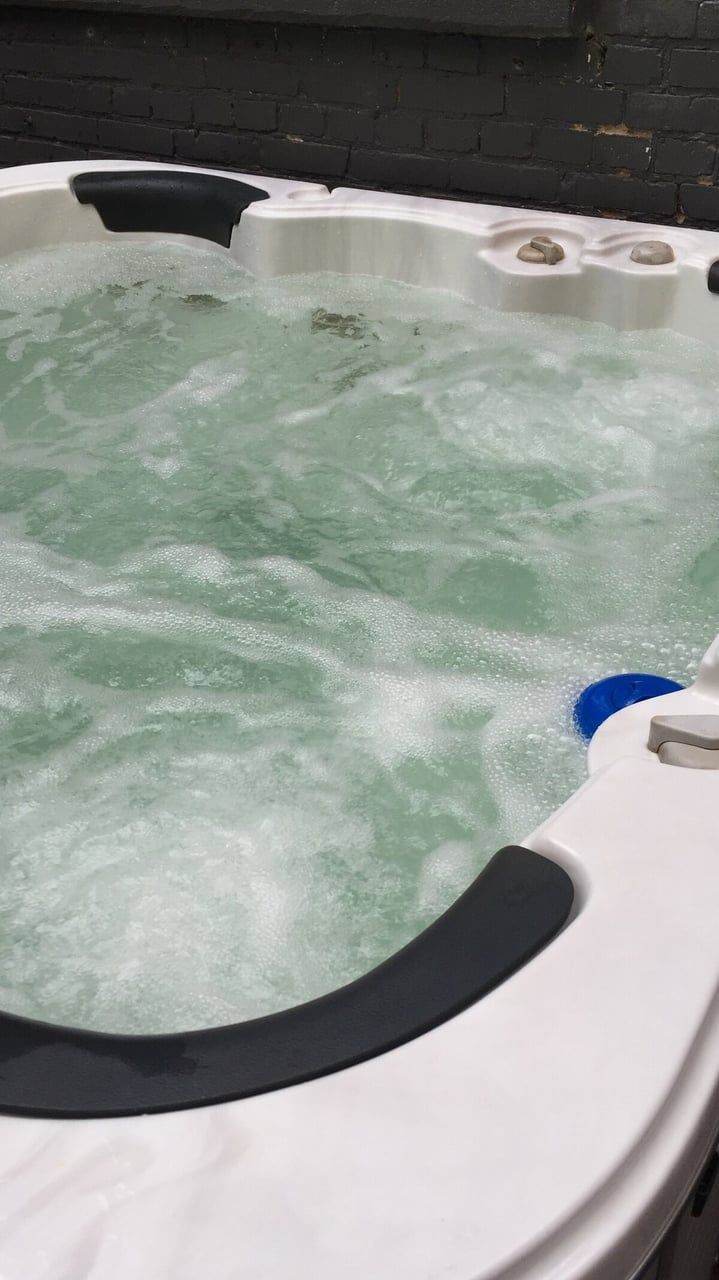 A hot tub with visible bubbles, a blue object, and a brick wall in the background.