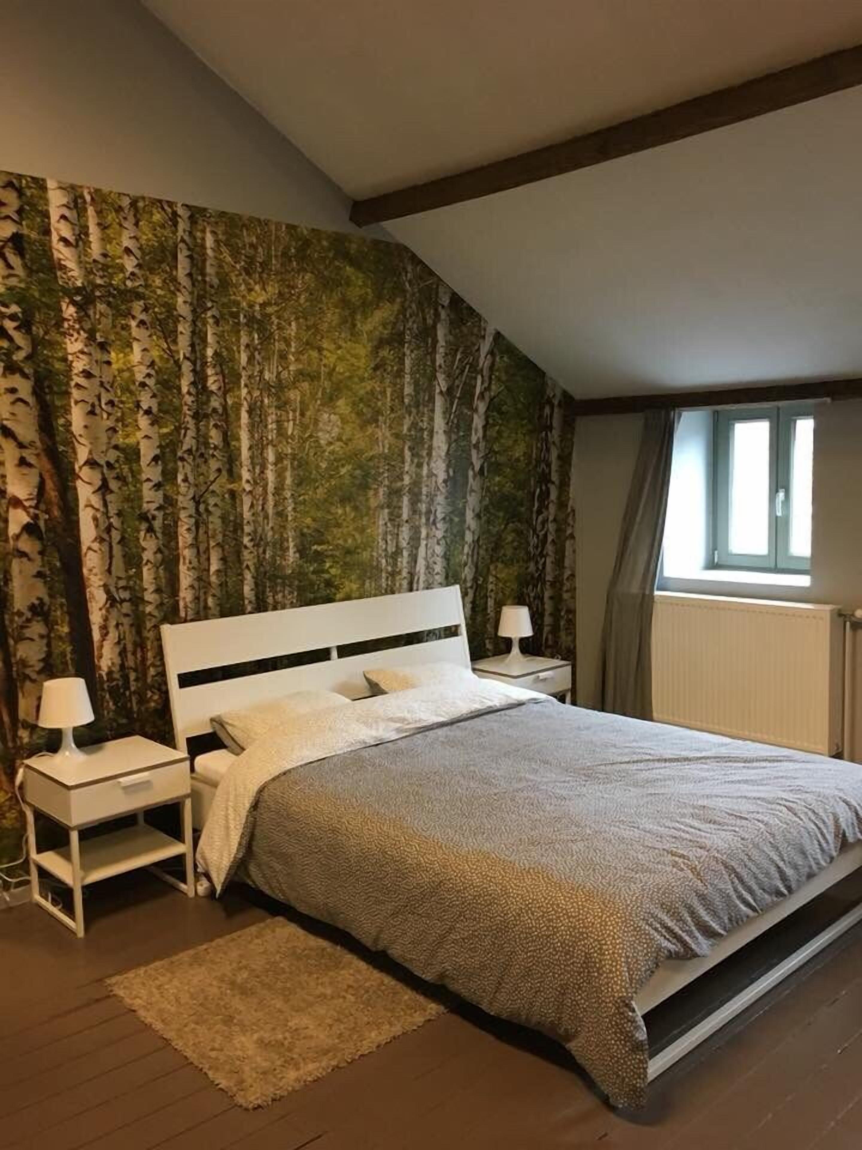 Une chambre à coucher avec un grand lit, une table de chevet, une lampe et une fenêtre avec des rideaux.