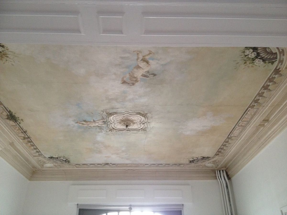 Een kamer met een hoge plafond, versierd met een decoratief fresco en een centraal medaillon.