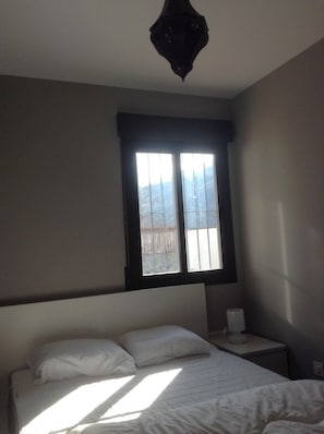 Quarto com cama, mesa de cabeceira, janela e luminária suspensa.