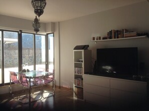 Una habitación con una mesa de comedor de vidrio, sillas, un televisor y una estantería.