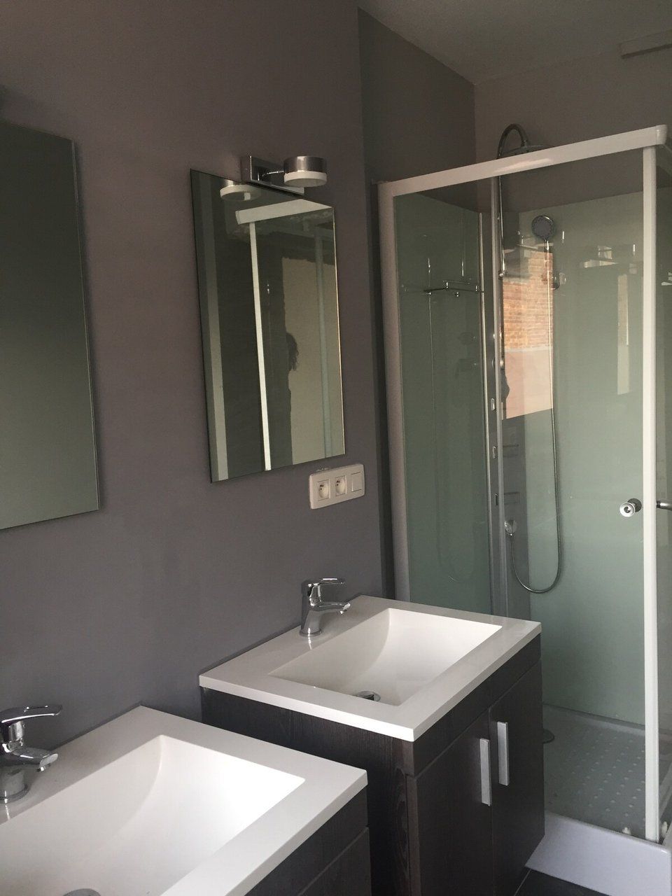 Een badkamer met twee wastafels, een spiegel en een douche met glazen wanden.