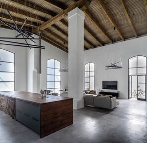 Un intérieur spacieux avec un plafond haut, de grandes fenêtres et un îlot central doté d’un comptoir en bois.