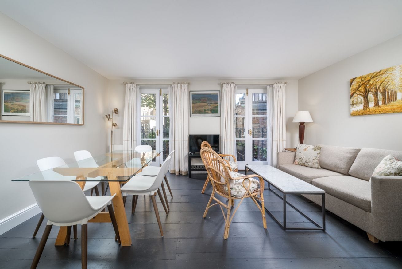 A modern living room with a glass dining table, white chairs, a sofa, and a fireplace.
