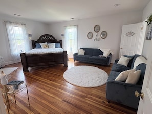 A bedroom with a wooden floor, a bed with a dark headboard, a blue sofa, and a white door. - 3 bedroom farmhouse located in the beautiful Shenandoah valley, just off I -81 (Staunton)