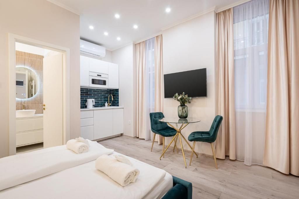 A hotel room with a bed, a desk, a chair, a TV, and a view of the kitchen.