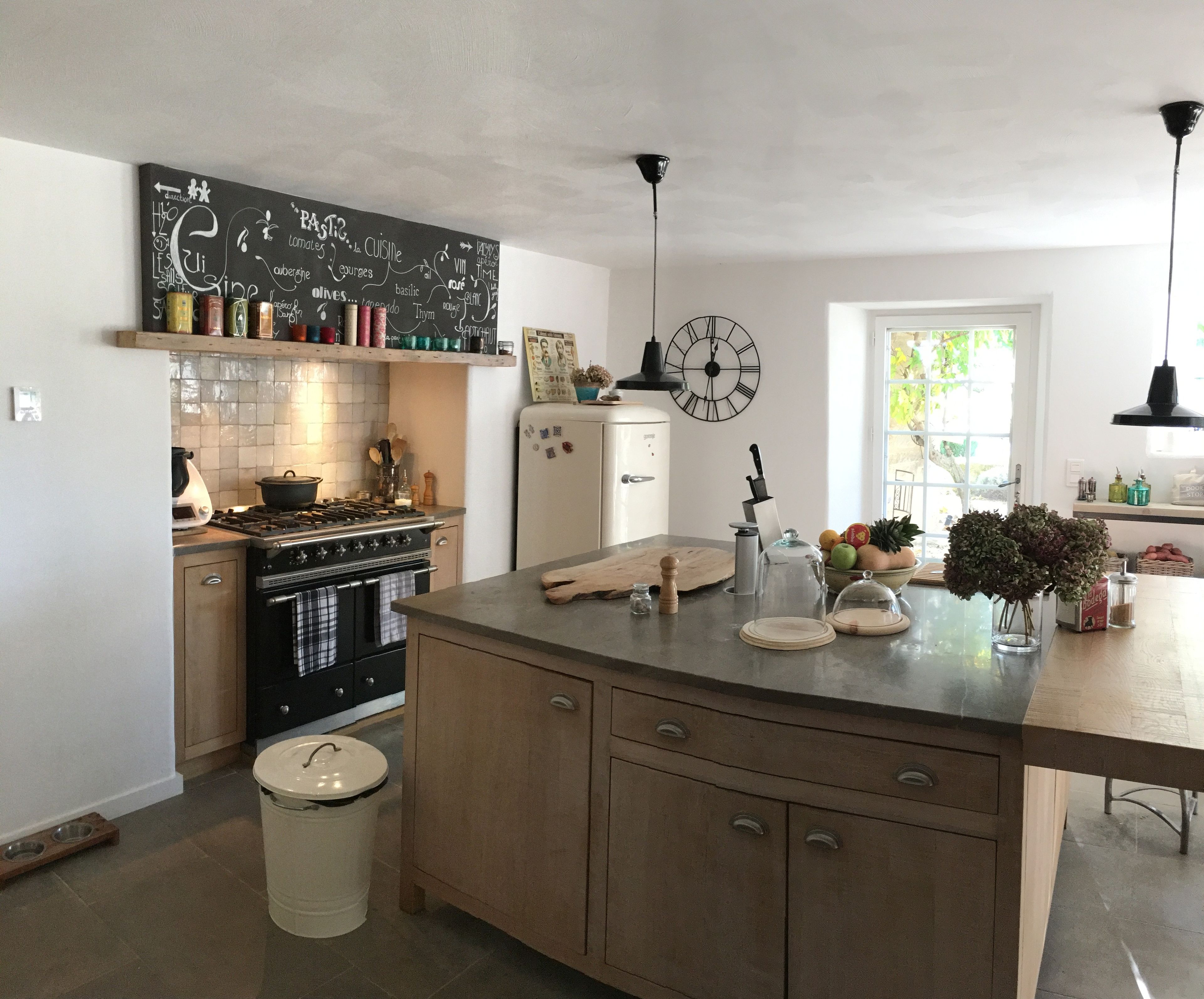 A kitchen with a central island, a stove, a refrigerator, and a chalkboard with food-related words.
