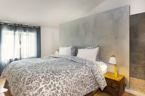 A bedroom with a bed, two bedside lamps, a large grey wall, and a window with curtains. - Farmhouse Amid Lavender - Heated Pool - Spa (La Baume-de-Transit)