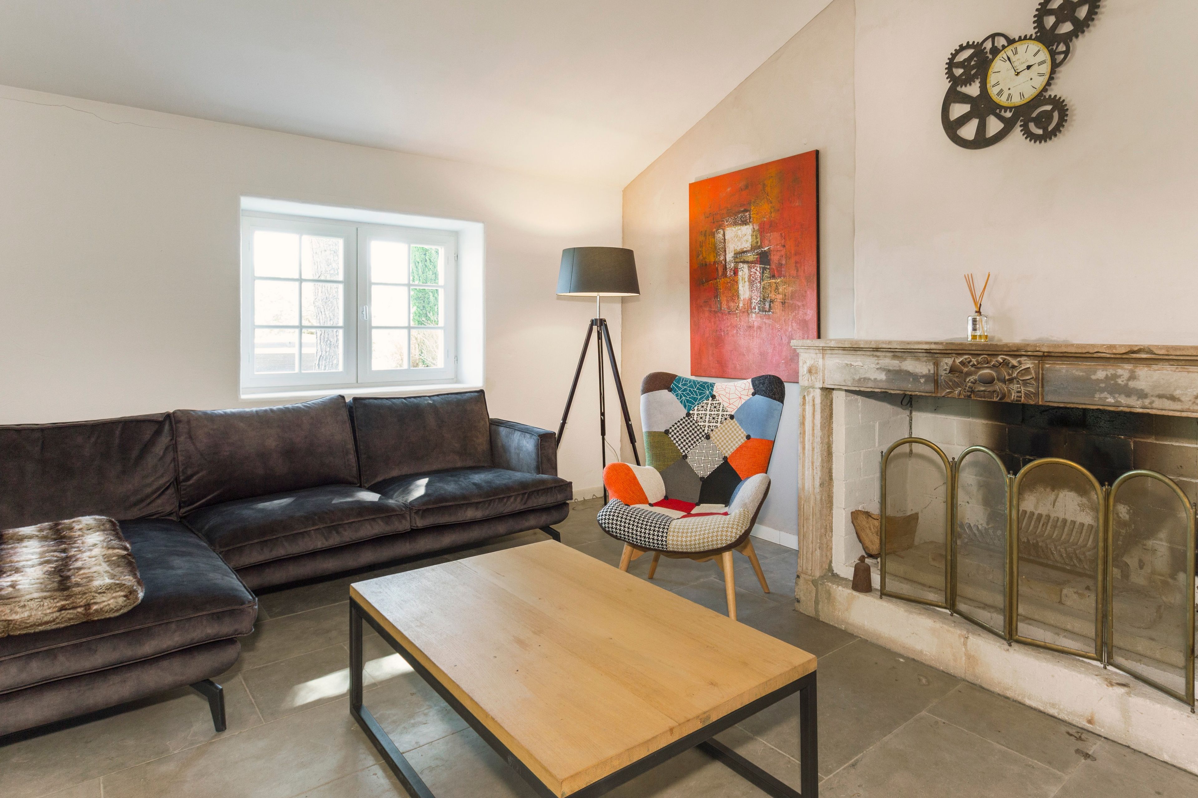 A living room with a sofa, a coffee table, a floor lamp, a colorful chair, a fireplace, and a wall clock.