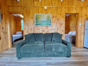 Une pièce aux murs en bois, avec un canapé vert et deux lits dotés de draps à motifs floraux.