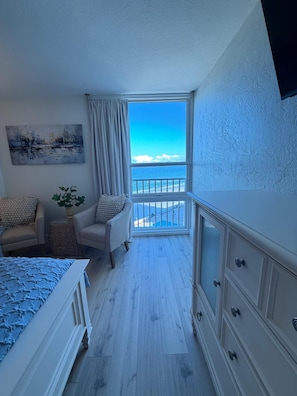 Ein Schlafzimmer mit Balkon, einem Bett, einem Sessel, einem Schminktisch und einem Bild an der Wand.